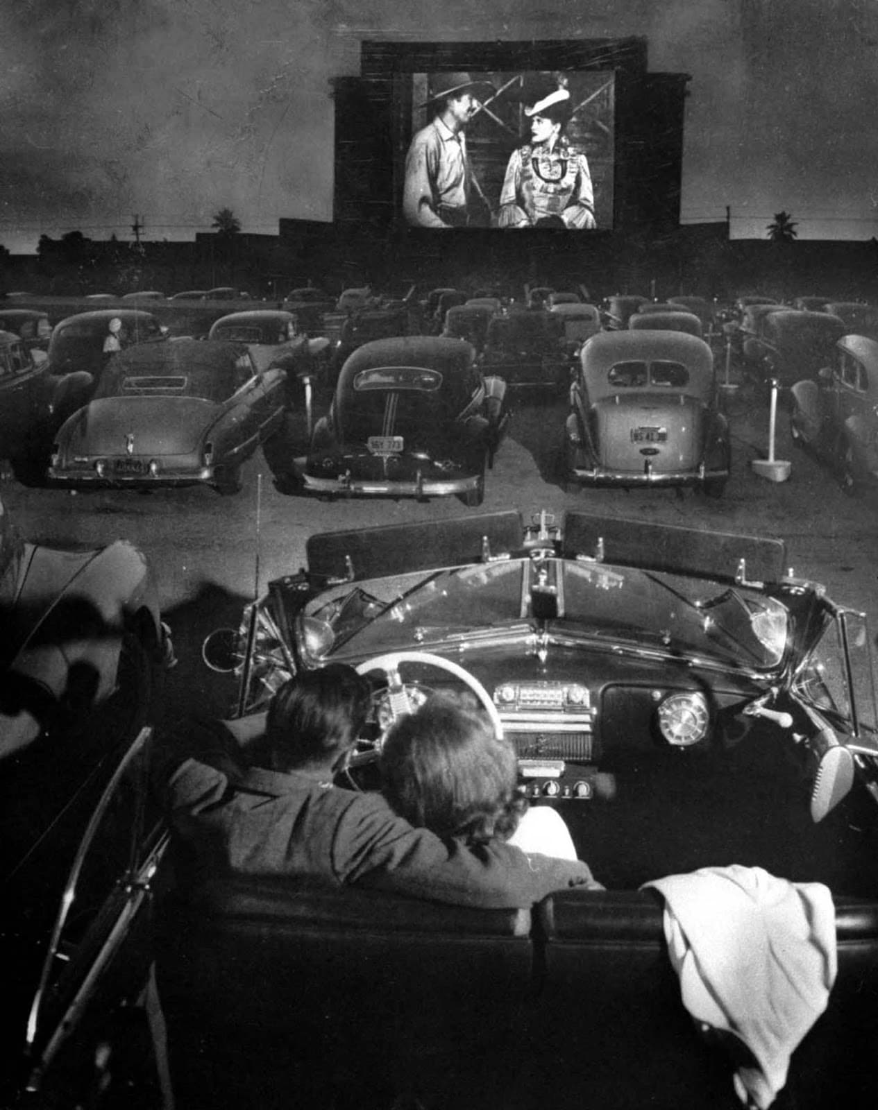 Cars lined up beneath the big outdoor screen.