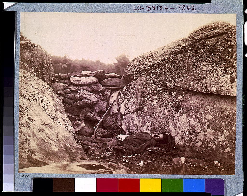 A fallen Confederate soldier behind a stone wall at Devil's Den, Gettysburg