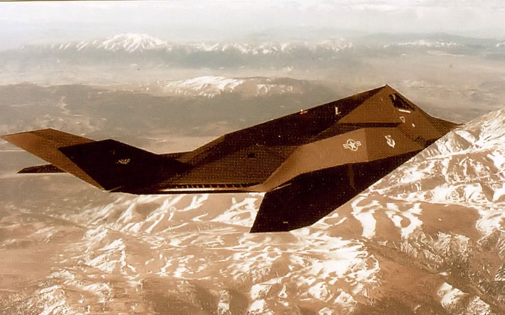 An F-117 Nighthawk stealth fighter flying over snow-capped mountains