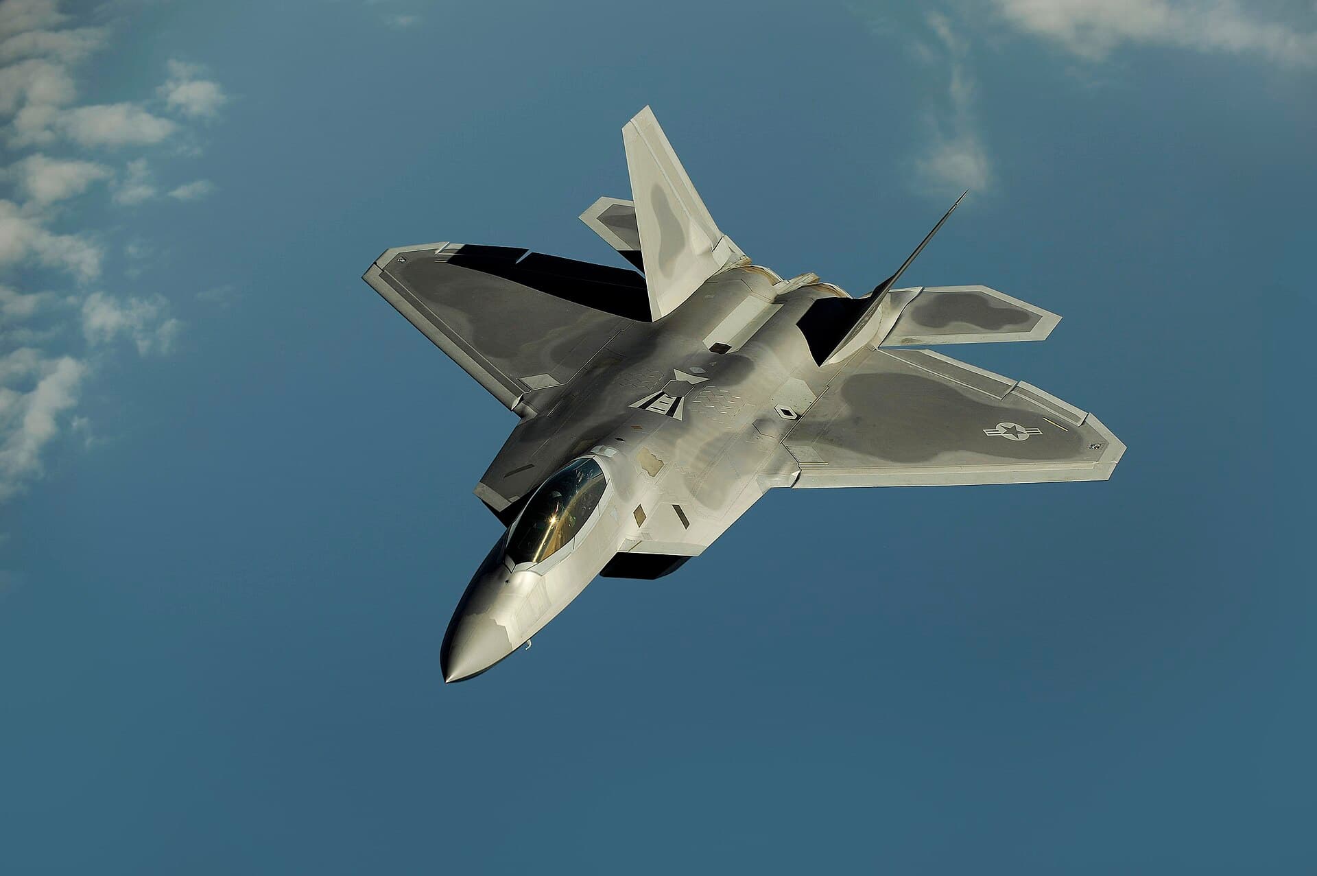 An F-22 Raptor stealth fighter banking against a blue sky