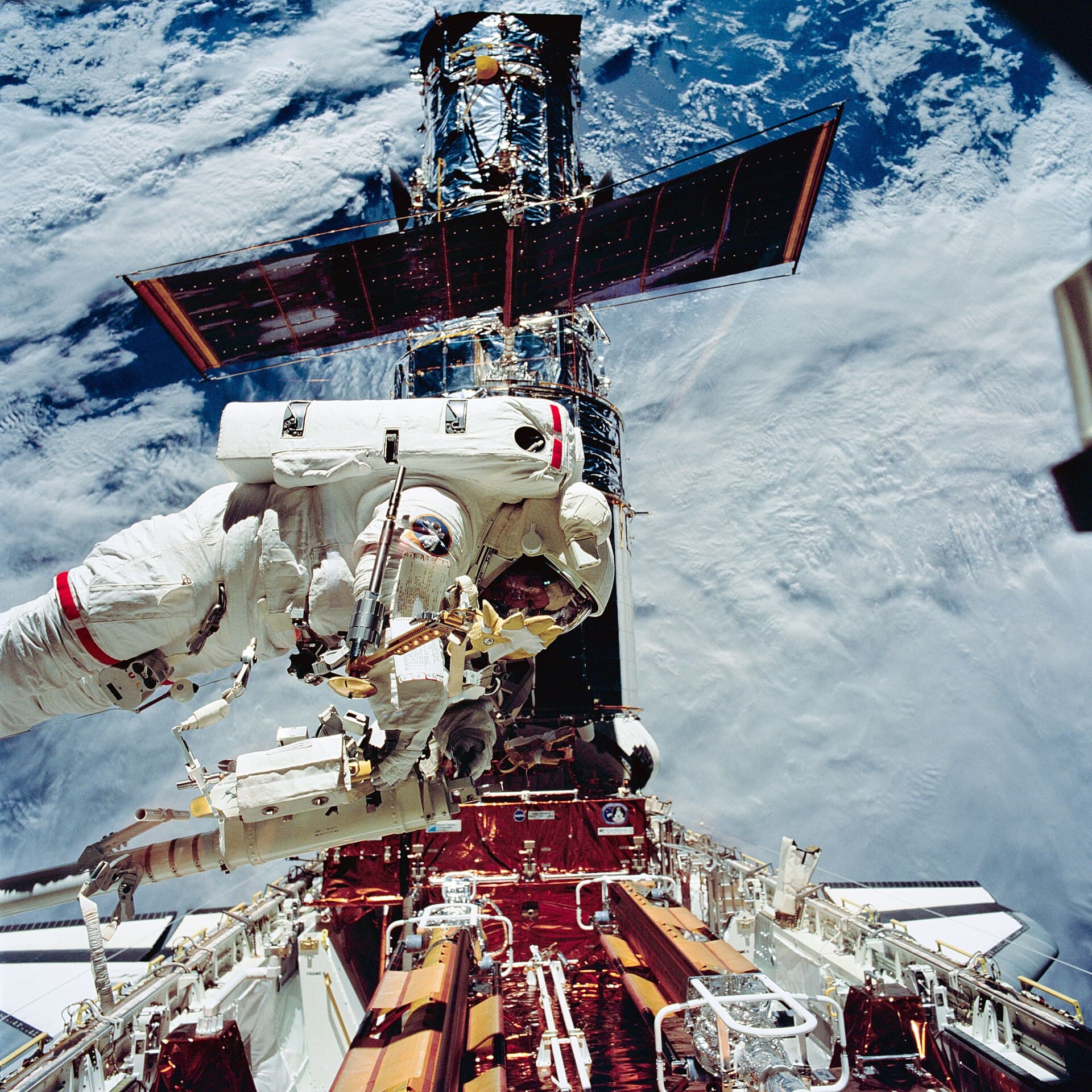 An astronaut servicing the Hubble Space Telescope on a spacewalk with Earth below