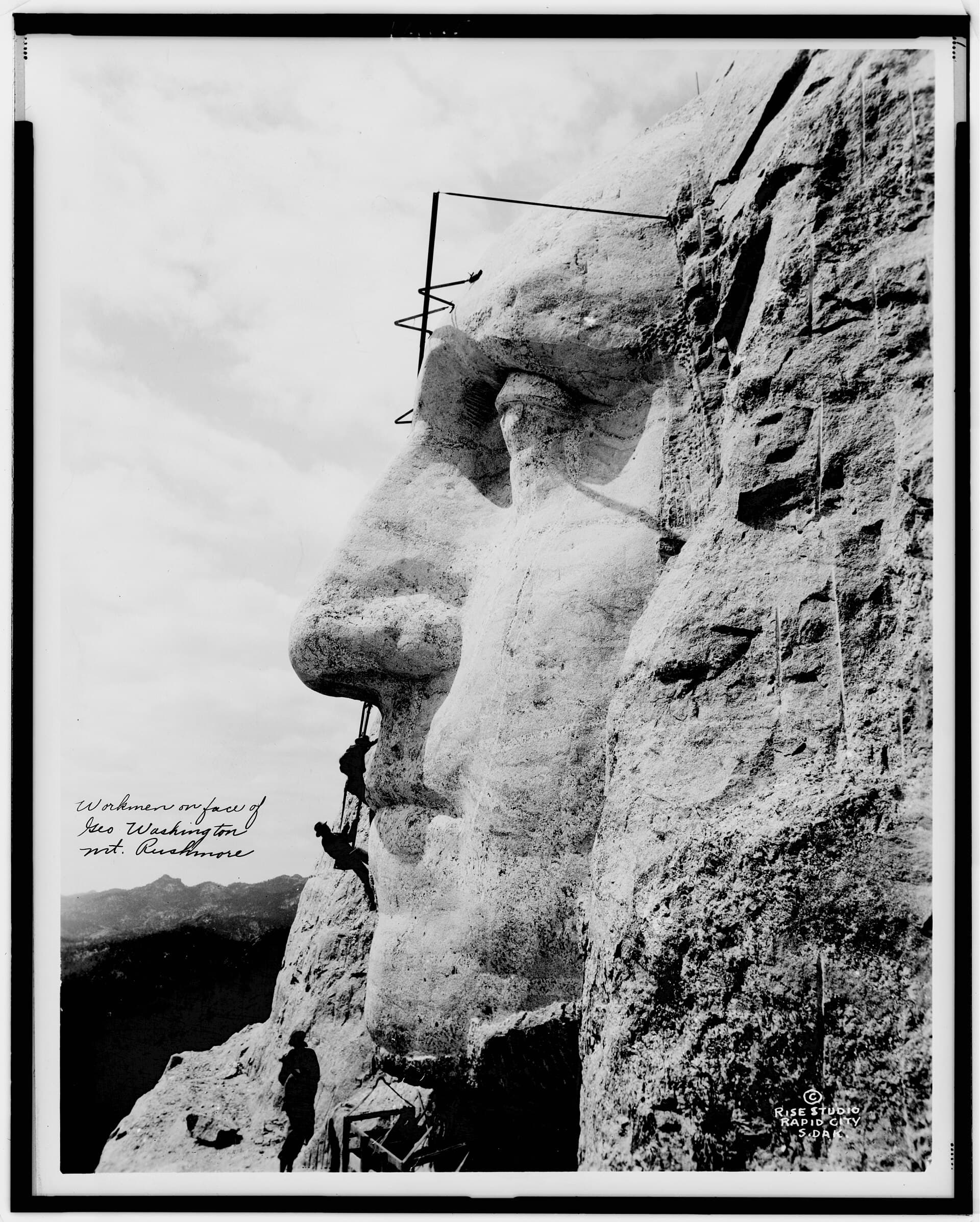 Workers on ropes carving the face of George Washington into Mount Rushmore