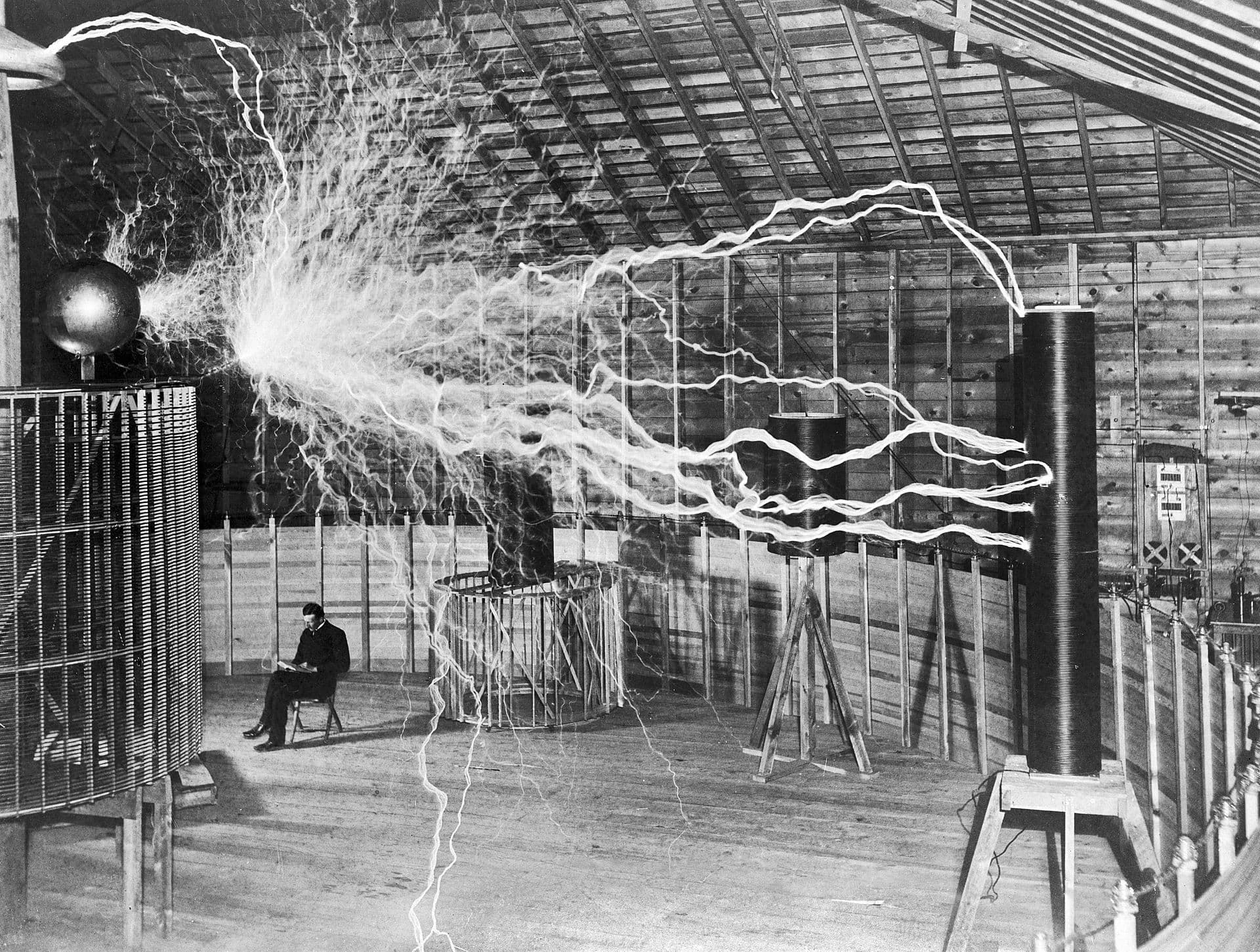 Nikola Tesla sitting calmly amid massive electrical arcs in his Colorado Springs laboratory