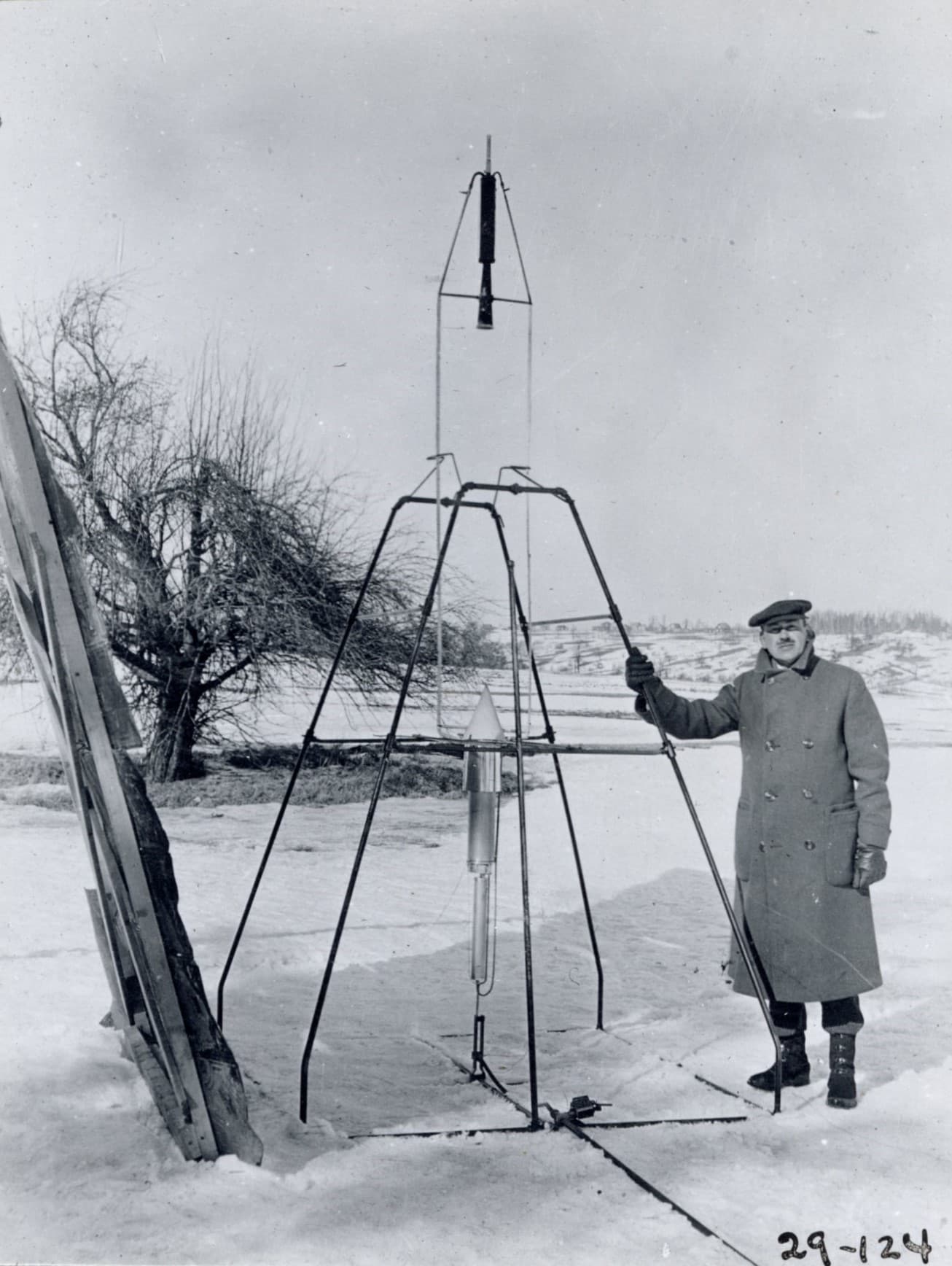 Robert Goddard standing beside his 1926 liquid-fueled rocket on its launch frame in the snow