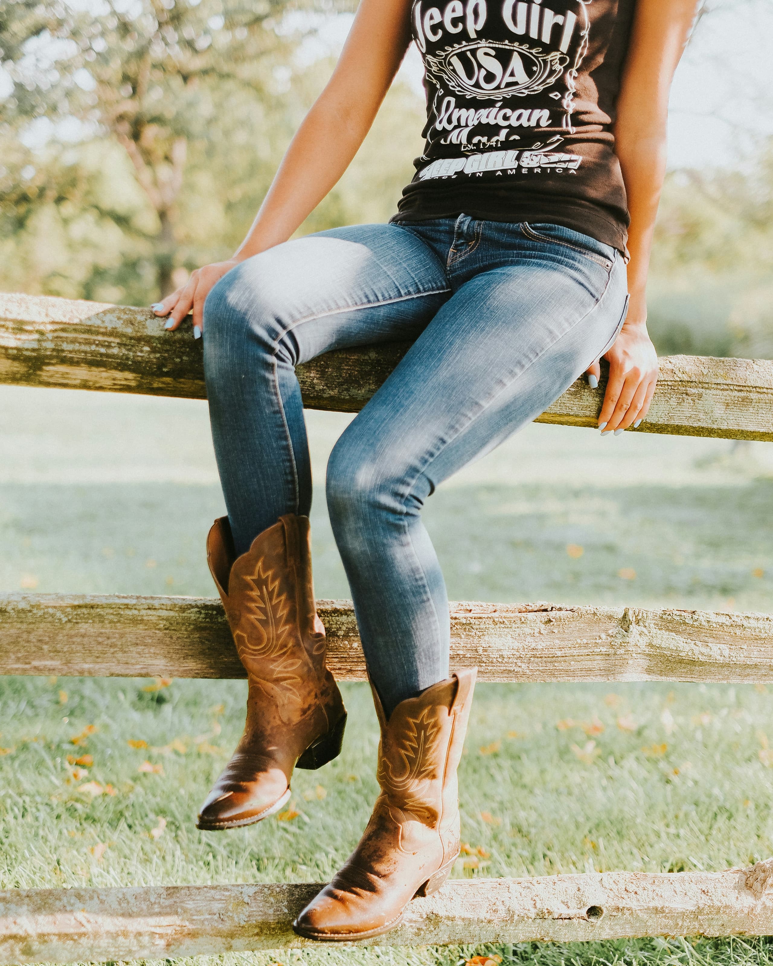Cowboy boots girl sitting on fence on ranch