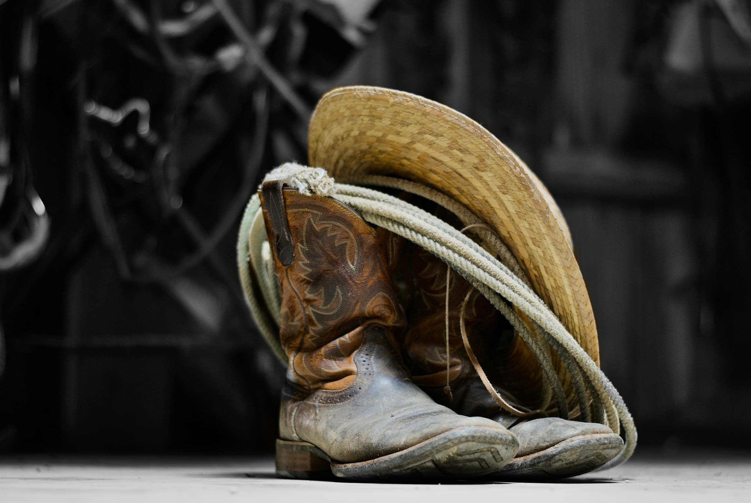 Worn square toe leather cowboy boots with coiled lasso rope and straw hat